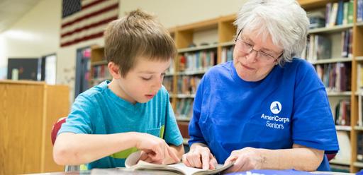 Lady wearing an AmeriCorps T-shirt reading with a small boy